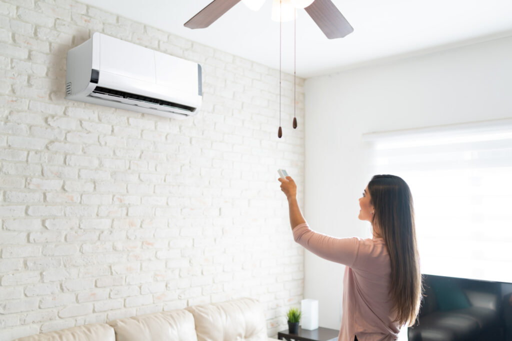 Homeowner using a remote to control a wall-mounted ductless mini-split system installed by Dowd Heating & Air Conditioning for efficient home comfort.