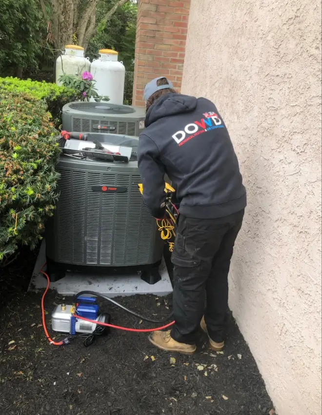 Dowd Heating & Air Conditioning technician performing maintenance on an outdoor air conditioning unit at a residential home to ensure reliable AC performance and efficiency.