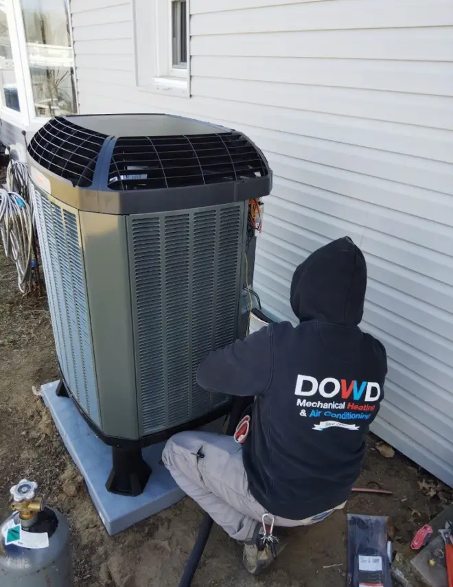 HVAC technician from Dowd Heating & Air Conditioning performing routine maintenance on an outdoor air conditioning unit as part of a residential HVAC maintenance plan to improve system performance and reliability.